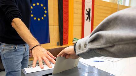 Stimmzettel-Einwurf in einem Berliner Wahllokal, im Hintergrund Europa-, Deutschland- und Berlin-Flaggen.