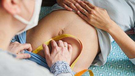 Mit einem Maßband misst eine Hebamme in ihrer Praxis den Symphysen-Fundus-Abstand bei einer schwangeren Frau. 