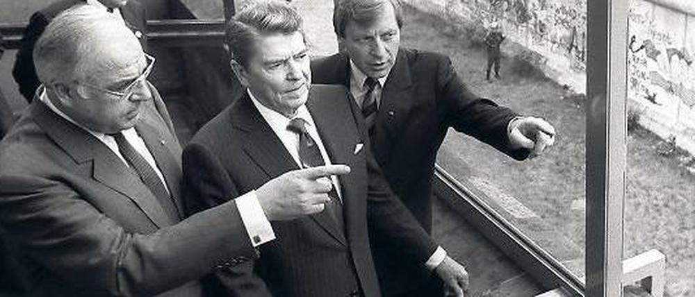 Noch 881 Tage. So lange dauerte es nach Reagans Besuch, bis die Mauer fiel. Hier wirft er vom Reichstag aus einen Blick darauf, flankiert von Kohl (li.) und Diepgen.
