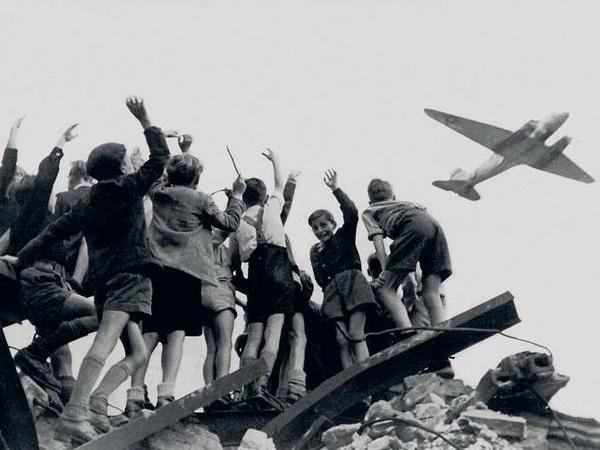 West-Berliner Jungen, die auf einem Trümmerberg stehen, begrüßen winkend ein US-amerikanisches Transportflugzeug, das während der Luftbrücke Versorgungsgüter nach West-Berlin bringt (Archivbild von 1948). 