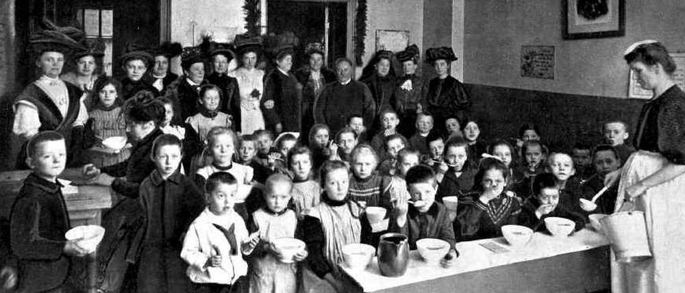 Eine Schar Kinder sitzt vor Suppenschüsseln in der Kreuzberger Kindervolksküche, von denen der jüdische Kaufmann Herrmann Abraham etwa ein Dutzend mit Spendengeldern betreibt.