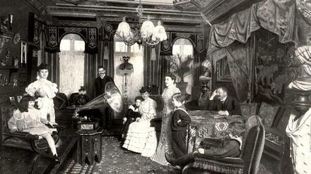In einem gediegen eingerichteten Wohnzimmer der Jahrhundertwende hat sich eine wohlhabende Berliner Familie um ein Grammophon versammelt.