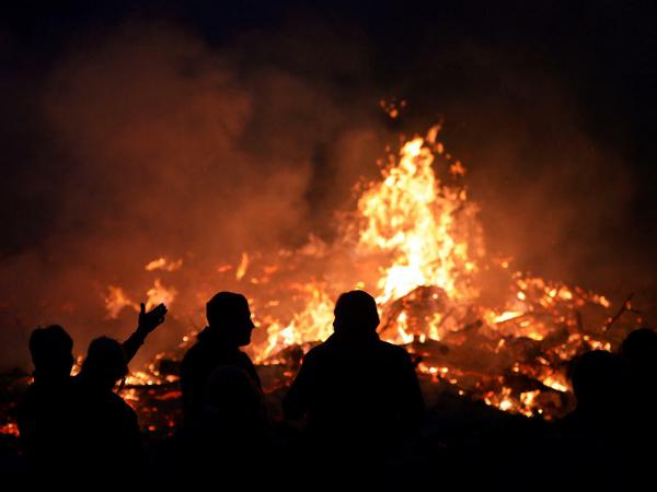 Die Flammen lodern. Menschen stehen an einem Osterfeuer.