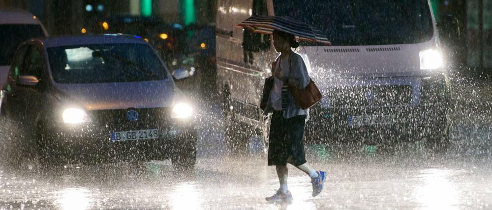 Eine Frau hält einen Regenschirm und läuft am Freitagabend in Berlin bei starkem Regenfall über eine Kreuzung.