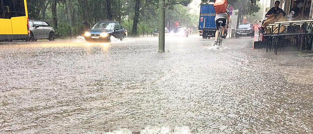 Wasser sprudelt Ende Juni in Berlin auf einer überfluteten Straße im Stadtteil Schöneberg aus einem Gully.