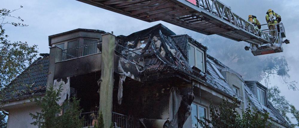 Zwei Feuerwehrleute löschen die letzten Flammen in einem Dachstuhl eines Hauses an der Goerzallee