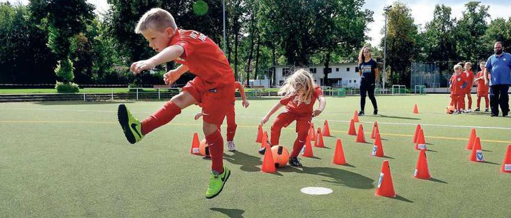Jungen und Mädchen spielen Fußball beim Feriencamp in Lichterfelde. Im Hintergrund Trainerin Vicdan Yavas und Trainer Alexander Regh. 