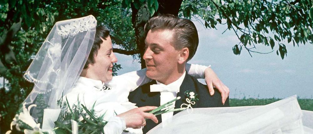 Das Bild aus dem Jahr 1957 zeigt einen Bräutigam im schwarzen Frack, der seine Braut im weißen Brautkleid, mit Strauß und Schleier, auf Händen trägt.
