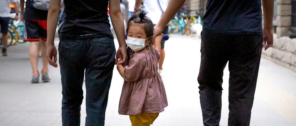 Ein kleines Mädchen mit Mundschutz wird auf ihrem Roller über einen Gehweg in Peking gezogen.