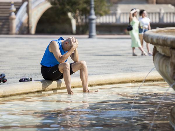Ein Mann kühlt sich im zentralen Brunnen auf der Plaza de España in Sevilla (Spanien) ab. 