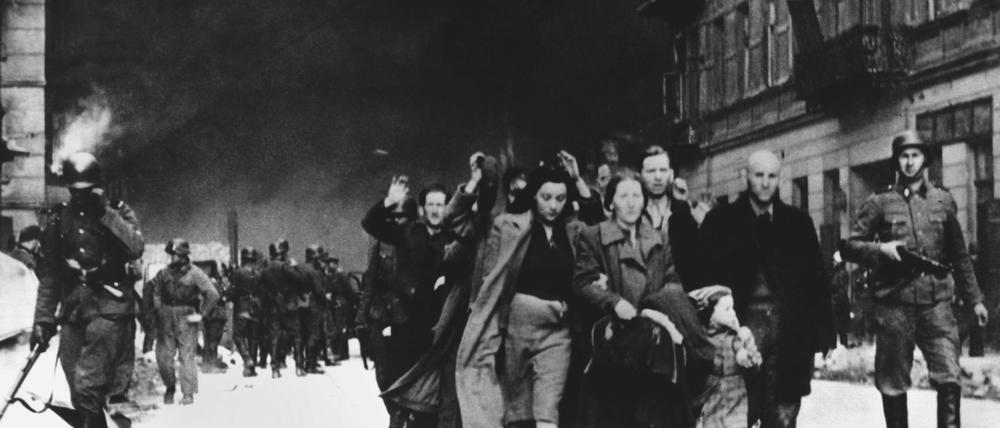 Mit erhobenen Händen werden im Mai 1943 jüdische Frauen, Männer und Kinder von deutschen SS-Soldaten aus dem brennenden Ghetto der polnischen Hauptstadt Warschau getrieben.