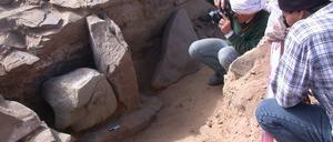 Kopfunter „bestattet“: Erste fotografische Dokumentation des Statuenkopfes 2004 in der Oase Tayma in Saudi Arabien. Der Entdecker, DAI-Archäologe Arnulf Hausleiter, ist rechts im Bild, mit Kamera und weißem Turban.