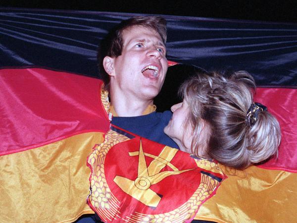 Ein jubelnden Paar am Tag der Deutschen Einheit mit einer DDR-Fahne (Archivbild vom 03. Oktober 1990 in Berlin).