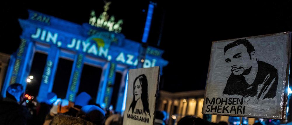 Activists display placards featuring portraits of recently executed Iranian demonstrator Mohsen Shekari (R), and Kurdish woman Mahsa Amini who died in police custody, during a demonstration in support of demonstrators in Iran, in front of the Brandenburg Gate illuminated with the words "Woman, Life, Freedom" in various languages including Kurdish and Persian, in Berlin on December 13, 2022. (Photo by John MACDOUGALL / AFP)