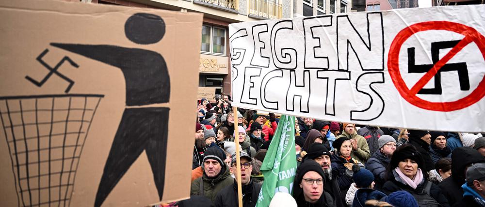 Demonstranten halten während einer Demonstration gegen Rassismus und rechtsextreme Politik in Frankfurt am Main am 20. Januar 2024 Plakate mit einem weggeworfenen und einem durchgestrichenen Hakenkreuz in der Hand.