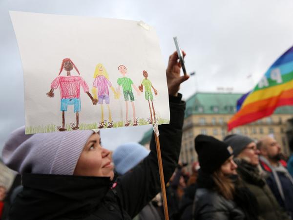 Kunterbunte Menschenkette. Eine Demonstrantin hält am 21. Januar 2024 in Berlin eine Kinderzeichnung mit abgebildeten Menschen hoch. 