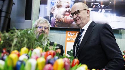 Kein Gras weit und breit: Ministerpräsident Dietmar Woidke (rechts, SPD) und Landwirtschaftsminister Axel Vogel (Grüne) stehen hinter Kunstblumen in der Brandenburg-Halle bei der Grünen Woche in Berlin.