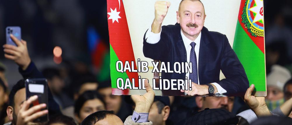 Menschen in Baku (Aserbaidschan) halten ein Plakat des Präsidenten in die Höhe.