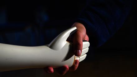 Eine menschliche Hand greift die Hand eines humanoiden Roboters.