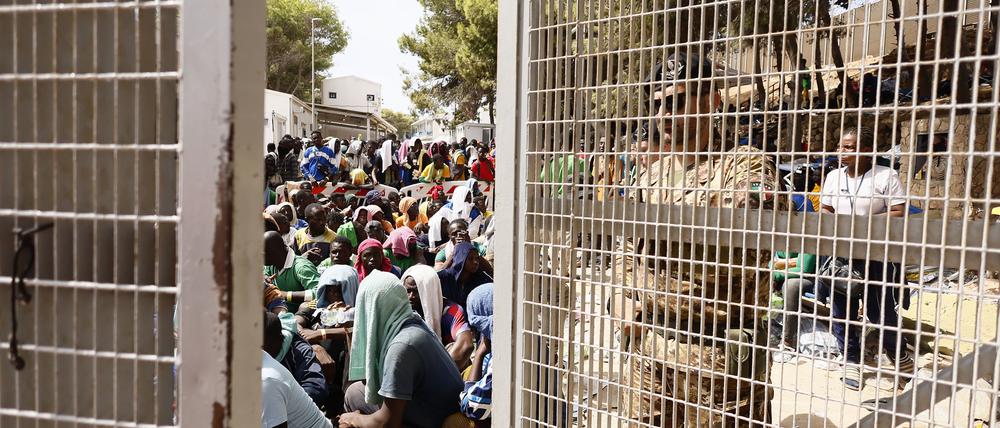 Ein Armeeoffizier schließt das Tor eines Auffanglagers für Migranten auf Lampedusa, während Migranten im Inneren sitzen. 