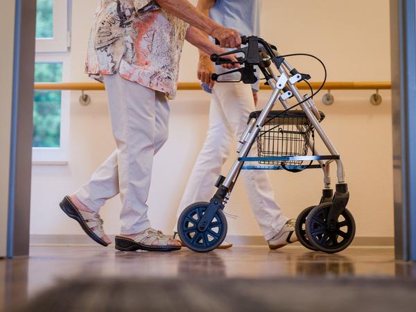 Eine Pflegekraft geht in einem Pflegeheim in Stuttgart mit einer älteren Dame über einen Korridor. 