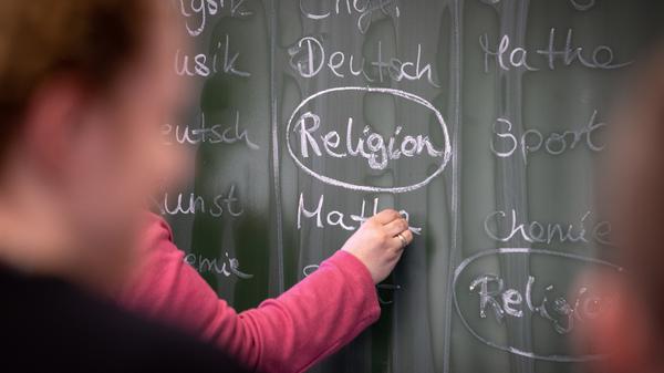ARCHIV - 14.02.2019, Nordrhein-Westfalen, Herford: ILLUSTRATION - Eine Lehrerin schreibt mit Kreide einen Stundenplan mit Religionsunterricht an eine Tafel. (zu dpa: «Nur noch zwei von drei Schulkindern besuchen Religionsunterricht») Foto: Friso Gentsch/dpa +++ dpa-Bildfunk +++