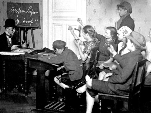 „Unser Lehrer ist doof“ steht auf der Tafel – schon um 1920, als das Foto der Schule spielenden Kinder entstand, war das ein beliebter Spaß für die Jugend. 