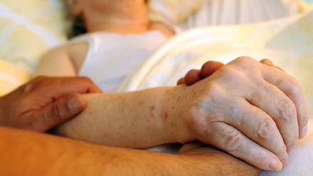 Ein Pfleger hält die Hand einer Frau. (Symbolbild)