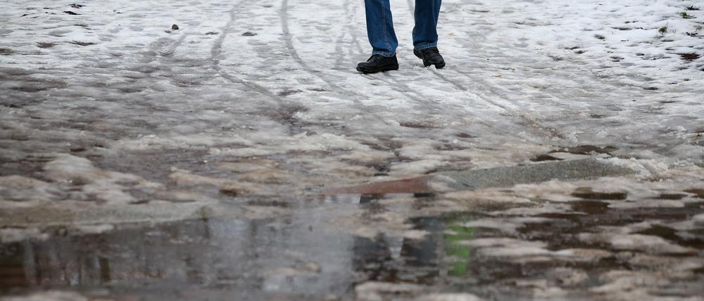 Ein Mann in Leipzig geht durch Schneematsch. In der Nacht stiegen die Temperaturen in die Plusgrade und es setzte Tauwetter ein. 