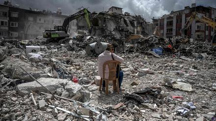 Eine Frau sitzt auf einem Stuhl in der Nähe ihres Hauses, während die Trümmer der eingestürzten Gebäude beseitigt werden.
