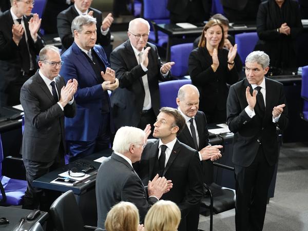 Frankreichs Präsident Emmanuel Macron wirft einen Kuss Richtung Ehrentribüne, auf der die ehemalige Bundeskanzlerin Angela Merkel sitzt. 