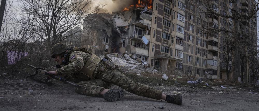 Ein ukrainischer Polizist geht vor einem brennenden Gebäude, das bei einem Luftangriff getroffen wurde, in Awdijiwka in Deckung. 