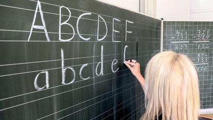 Eine Grundschullehrerin schreibt die ersten Buchstaben des Alphabets auf eine Schultafel in einem Klassenzimmer. 
