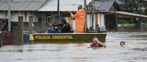 Polizeibeamte kontrollieren ein Haus, während Anwohner über eine überschwemmte Straße im Bundesstaat Rio Grande do Sul waten, nachdem ein Unwetter Überschwemmungen verursacht hat. Bei schweren Unwettern im Süden Brasiliens sind mindestens 36 Menschen ums Leben gekommen. 
