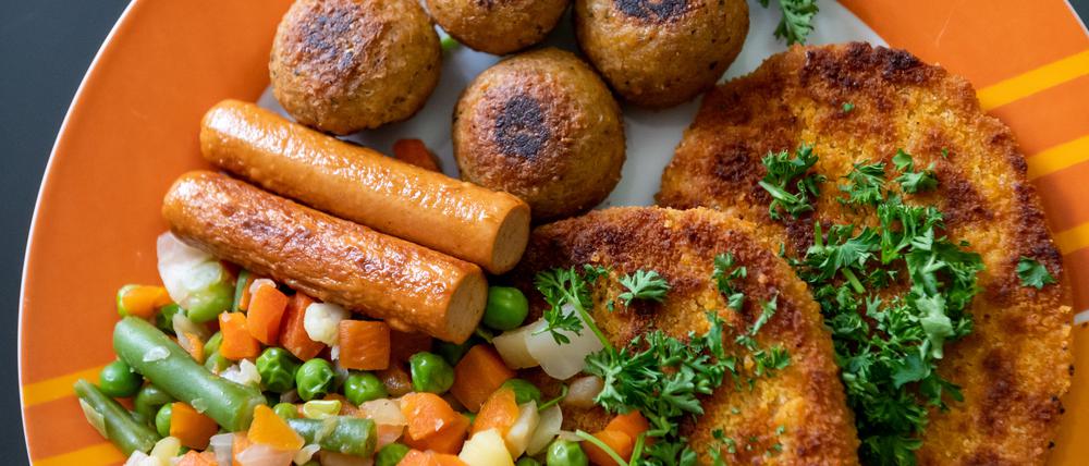 Vegane Falafel, vegane Schnitzel, vegane Würstchen und Gemüse sind auf einem Teller in einer Küche zu sehen.