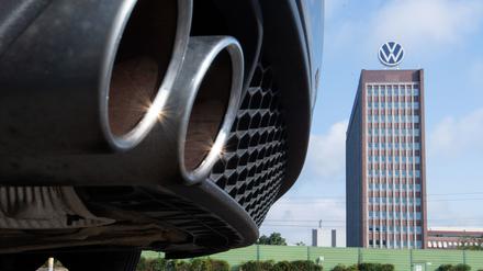 Auspuffrohre eines Volkswagen, fotografiert mit dem Markenhochhaus am VW-Werk Wolfsburg im Hintergrund.