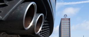 Auspuffrohre eines Volkswagen, fotografiert mit dem Markenhochhaus am VW-Werk Wolfsburg im Hintergrund.
