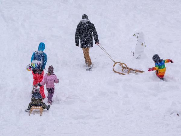 Erwachsene mit Kindern und Schlitten gehen den Hügel hinter dem Landtag in München hinauf, nachdem es stark geschneit hat.