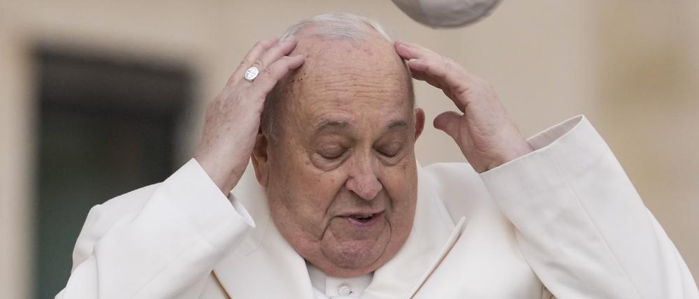 Papst Franziskus versucht am Mittwoch im Vatikan, seine Mütze aufzufangen, die der Wind weggeweht hat, als er zu seiner wöchentlichen Generalaudienz auf dem Petersplatz kommt.
