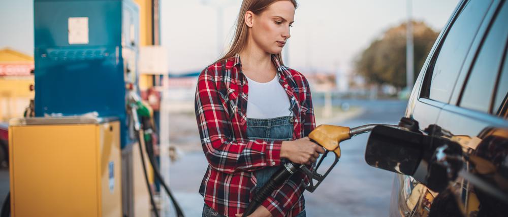 Eine Frau betankt an einer Tankstelle sein Auto. 