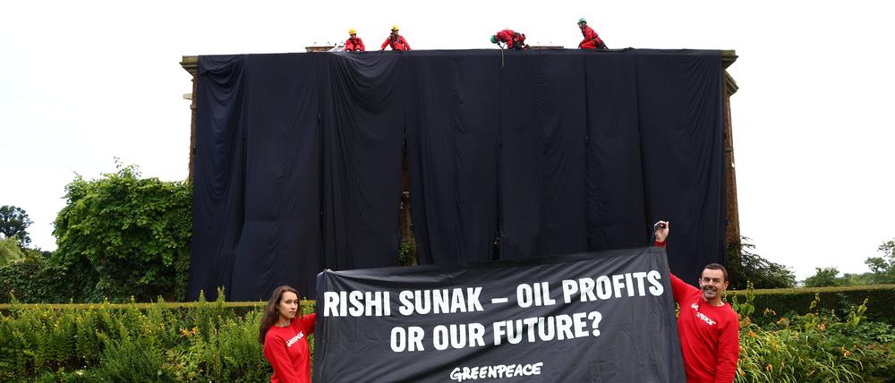 Greenpeace-Aktivisten haben ein Haus verhüllt und halten ein Plakat mit der Aufschrift „Rishi Sunak –  Ölprofite oder unsere Zukunft?“