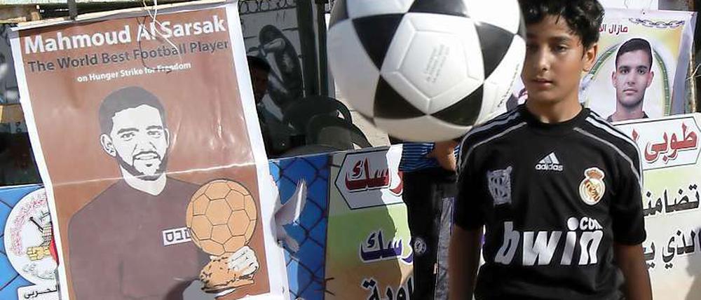 Ein palästinensischer Junge spielt Fußball neben einem Plakat, das Mahmoud Sarsak zeigt. In Palästina wird regelmäßig für die Freilassung des ehemaligen Nationalspielers demonstriert. Nun, da Europa im Fußballfieber ist, findet sein Fall auch international Beachtung.