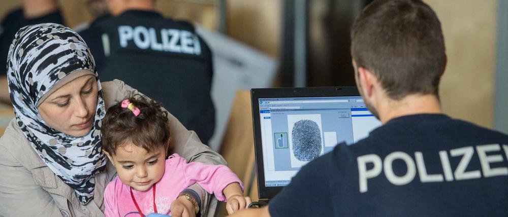 Ein Beamter der Bundespolizei nimmt am 14.07.2015 im Notquartier der Bundespolizeiinspektion in Passau (Bayern) mit einem Scanner Fingerabdrücke von der syrischen Flüchtlingsfrau Delal mit ihrer Tochter. Die Zahl illegaler Einreisen nach Deutschland steigt rasant und stellt die Bundespolizei vor wachsende Probleme. 