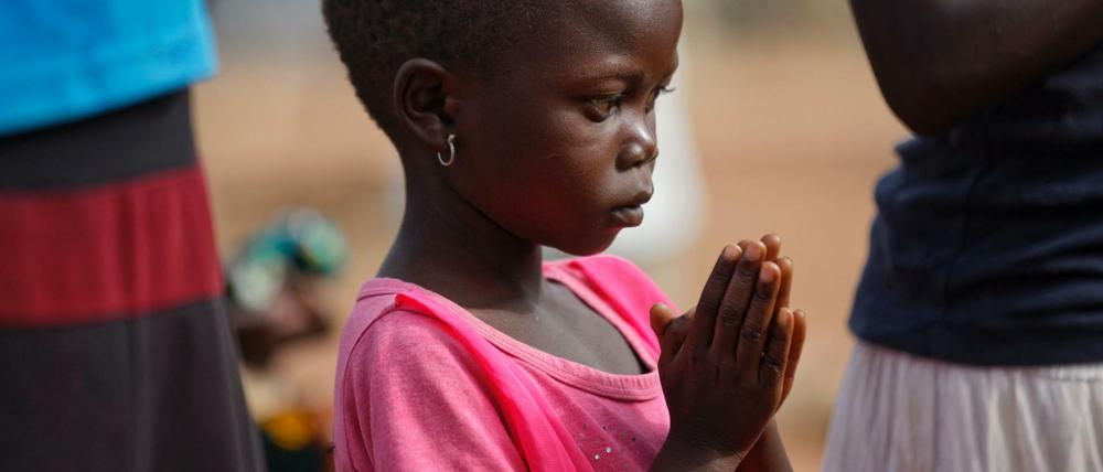 Ein betendes Flüchtlingsmädchen aus dem Südsudan. Die gläubigen Christen halten den Gottesdienst unter freiem Himmel ab. 