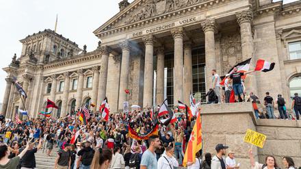 Teilnehmer einer Kundgebung gegen die Corona-Maßnahmen stehen auf den Stufen zum Reichstagsgebäude, zahlreiche Reichsflaggen sind zu sehen. 