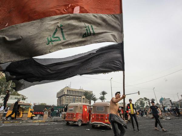 Irak, Bagdad: Ein regierungskritischer Demonstrant schwenkt bei Zusammenstößen mit den Sicherheitskräften auf dem Al-Khilani-Platz die irakische Flagge.