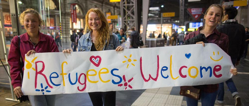 Die Stimmung in Deutschland vor zwei Jahren: Drei junge Frauen stehen in Frankfurt am Main im Hauptbahnhof mit einem Begrüßungsplakat.