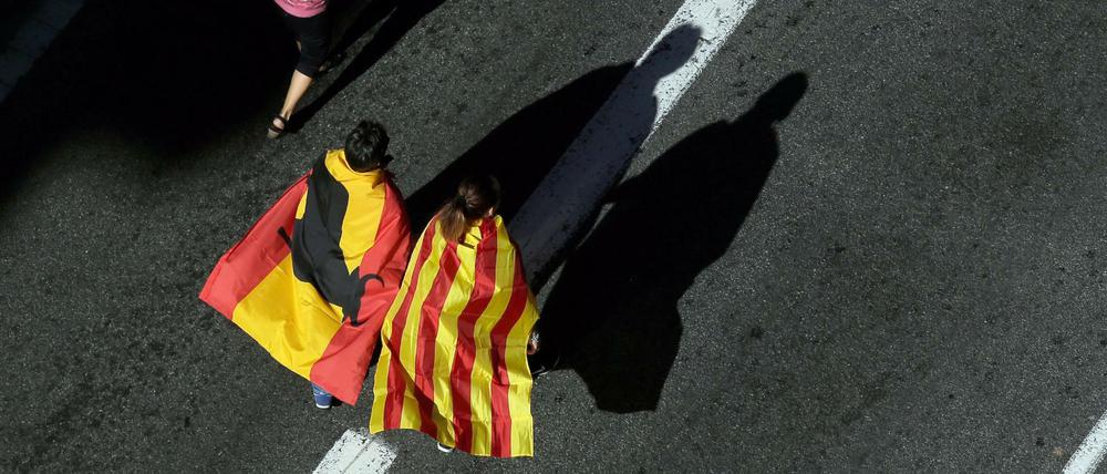 Nation und Region: Ein Mann und eine Frau mit einer spanischen und einer katalanischen Fahne um die Schulter gehen bei einem Protestmarsch in Barcelona (Spanien) eine Straße hinunter.