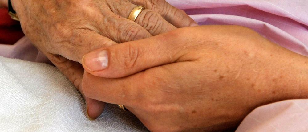 Eine Hospiz-Schwester hält die Hand einer todkranken Bewohnerin.