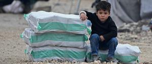 Ein syrischer Junge sitzt neben Säcken mit Hilfsgütern in einem Camp.